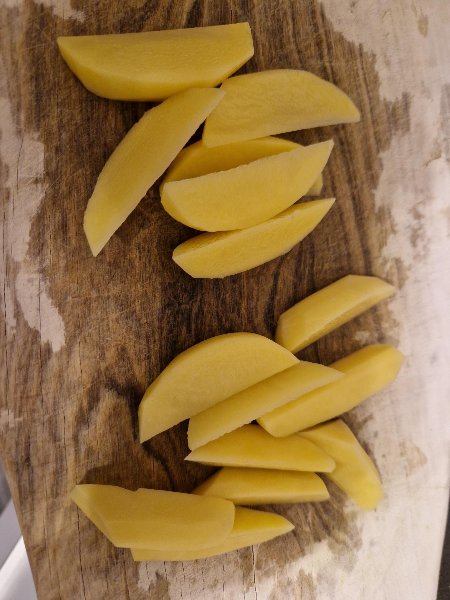 Geschälte Kartoffeln, in Spalten geschnitten, auf einem Holzbrett