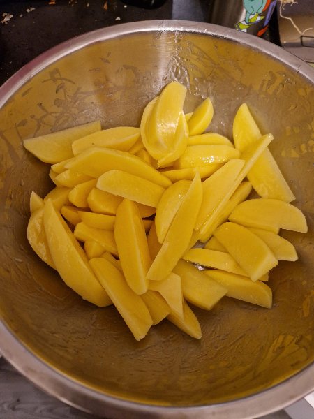 Kartoffelspalten mit Öl in einer Edelstahlschüssel