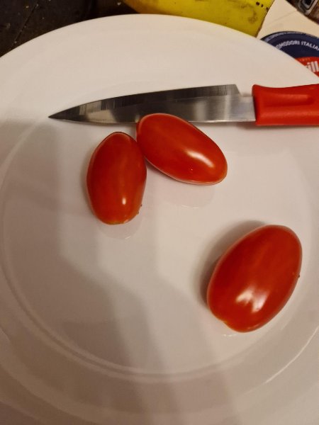 Drei kleine Tomaten und ein Messer auf einem Teller